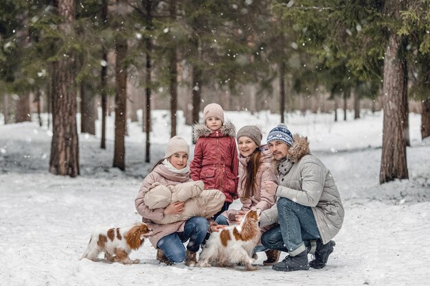 Une jeune famille caucasienne heureuse joue avec un chien en hiver dans une forêt de pins