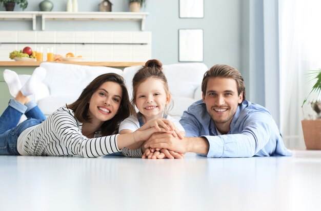 Une jeune famille caucasienne avec une petite fille pose se détendre sur le sol dans le salon, une petite fille souriante embrasse ses parents, montre de l'amour et de la gratitude, se repose à la maison ensemble.