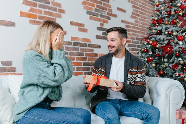 Une jeune famille célèbre ensemble le Nouvel An et Noël, un couple homme et femme se donnent des cadeaux assis sur un canapé à la maison heureux et amoureux