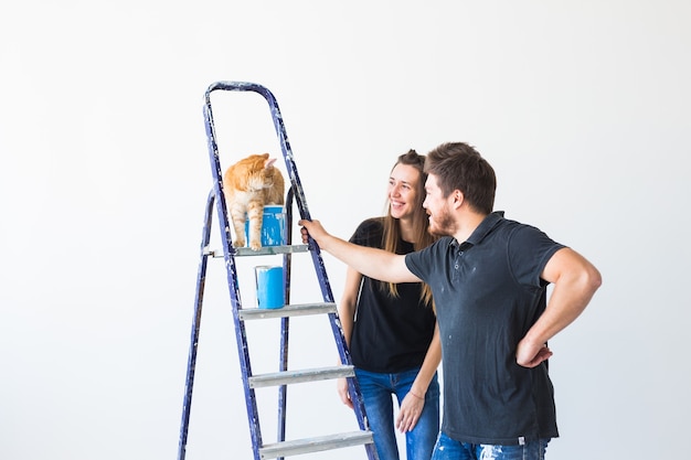 Jeune famille avec chat faisant la réparation et la peinture des murs ensemble et en riant.