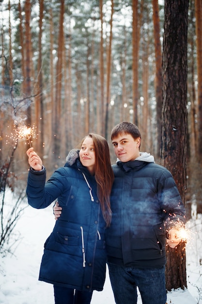 Jeune famille debout dans une forêt d'hiver avec des cierges pour une ambiance festive