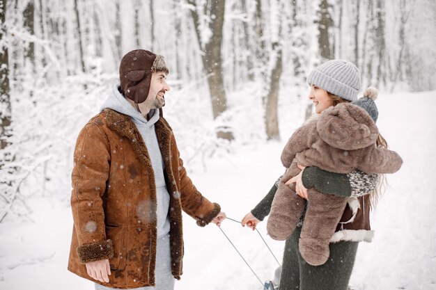 Jeune famille avec deux enfants à cheval sur un traîneau dans la forêt d'hiver