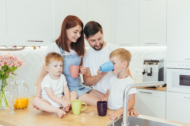 Jeune famille avec deux petits enfants prenant le petit déjeuner dans une belle cuisine blanche