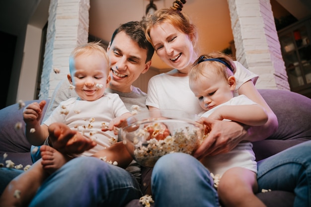 Jeune famille avec enfants mangeant du pop-corn sur le canapé à la maison