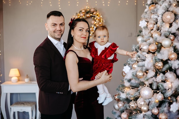 Jeune famille excitée faisant l'arbre de Noël ensemble à la maison, se préparant avant le réveillon de Noël