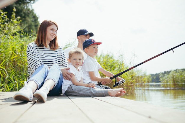 Jeune famille, femme homme et deux petits enfants pêchant sur le lac, mari et femme passent un bon week-end ensemble