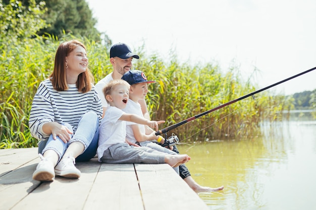 Jeune famille, femme homme et deux petits enfants pêchant sur le lac, mari et femme passent un bon week-end ensemble