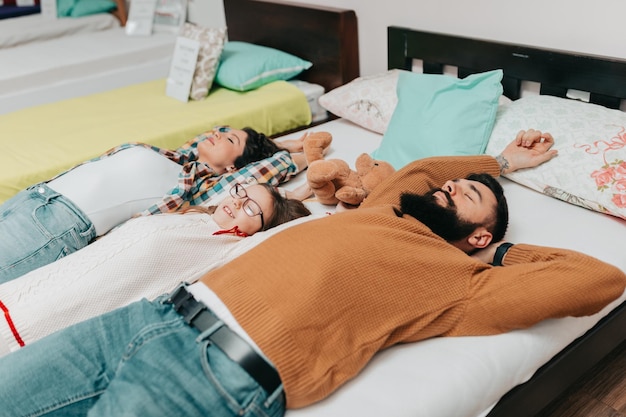 Jeune famille heureuse achetant un nouveau lit et matelas dans un grand magasin de meubles