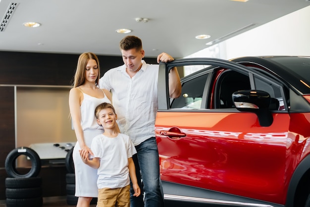 Une jeune famille heureuse choisit et achète une nouvelle voiture chez un concessionnaire automobile