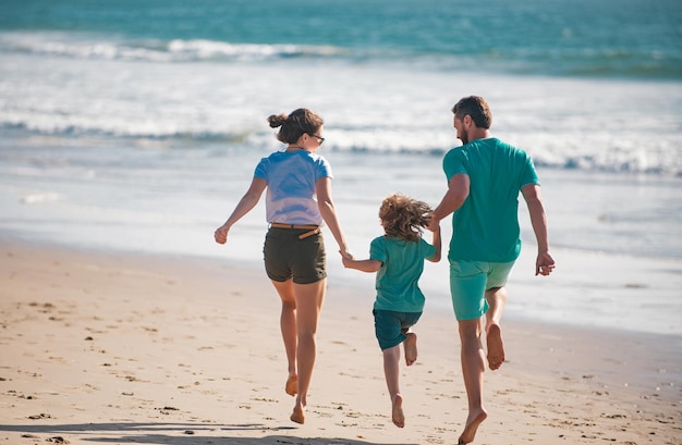 Photo une jeune famille heureuse court et saute sur la plage d'été. un enfant avec des parents qui courent et sautent en bonne santé.