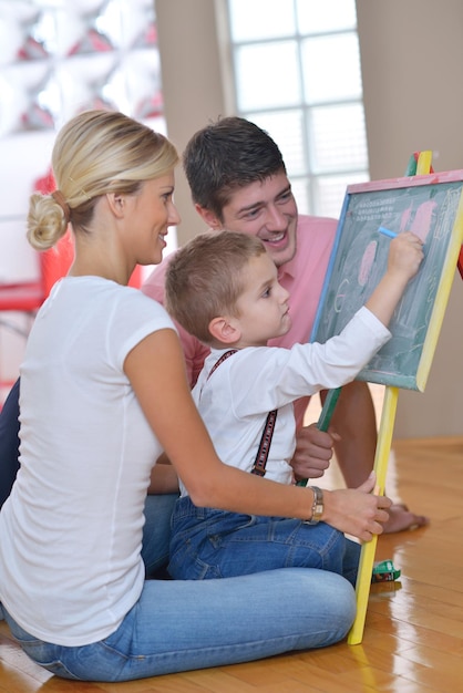 une jeune famille heureuse enseigne des leçons et prépare son fils à l'école tout en dessinant à bord à la maison