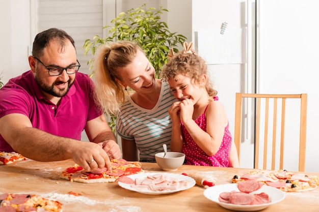 La jeune famille heureuse fait cuire la pizza faite maison