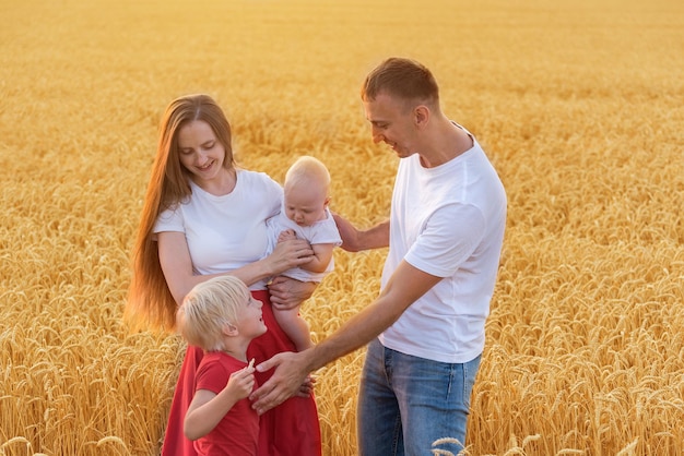 Jeune famille heureuse marchant dans le champ de blé mûr. Maman, papa et deux enfants s'amusant