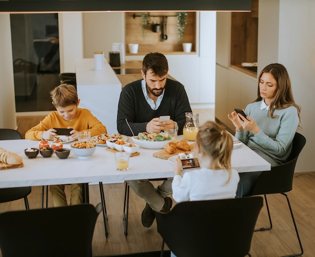 Jeune famille heureuse parlant tout en déjeunant à la table à manger de l'appartement