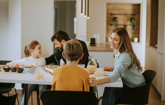 Jeune famille heureuse parlant tout en prenant le petit déjeuner à la table à manger de l'appartement