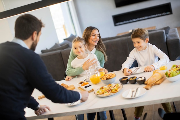 Jeune famille heureuse parlant tout en prenant son petit déjeuner à la table à manger de l'appartement