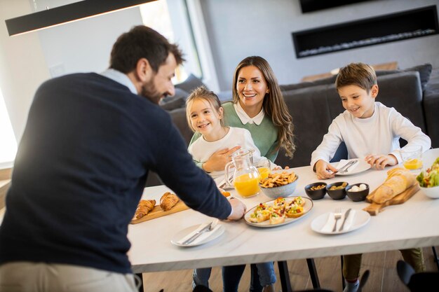 Jeune famille heureuse parlant tout en prenant son petit déjeuner à la table à manger de l'appartement