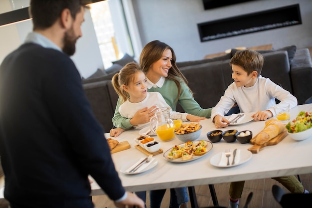 Jeune famille heureuse parlant tout en prenant son petit déjeuner à la table à manger de l'appartement