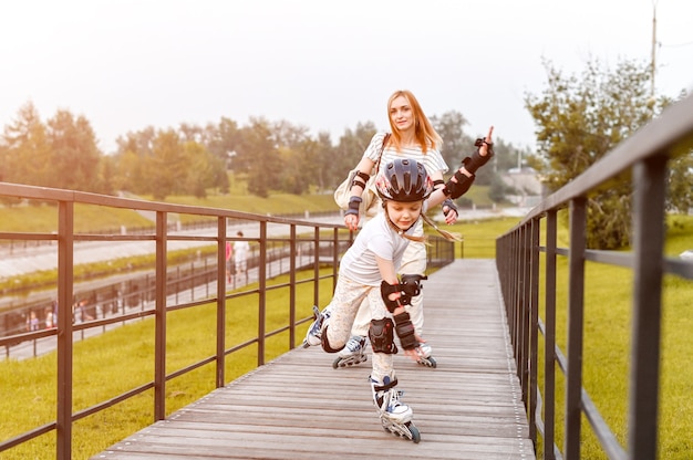 Photo jeune famille heureuse patinage à roulettes dans le parc. marche active. fille d'âge préscolaire ayant une marche active avec sa mère. focus dinamique