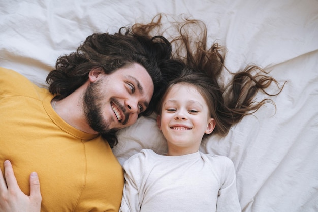 Jeune famille heureuse avec père barbu et fille sur le lit dans une maison confortable vue du haut