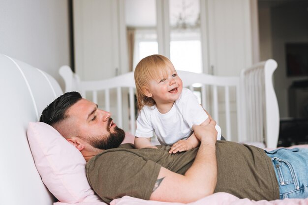 Jeune famille heureuse avec père et fille bébé fille sur le lit dans une maison confortable