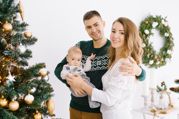 Une jeune famille heureuse avec un petit enfant fils fête la nouvelle année et fête Noël à l'arbre de vacances