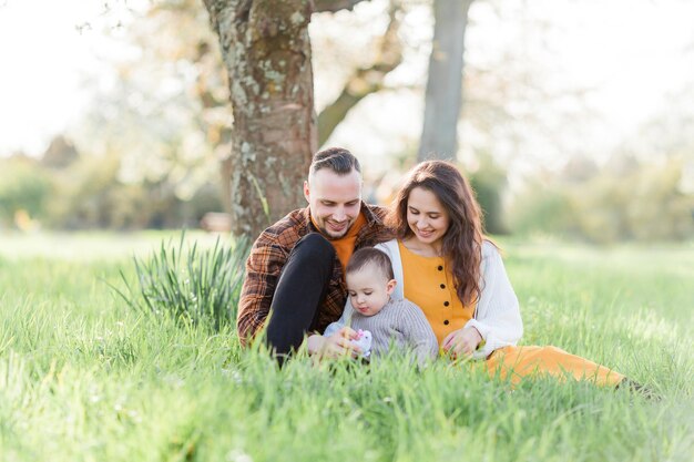 Une jeune famille heureuse avec un petit fils se promène dans un jardin fleuri Maman et papa avec un bébé de 1 an Printemps