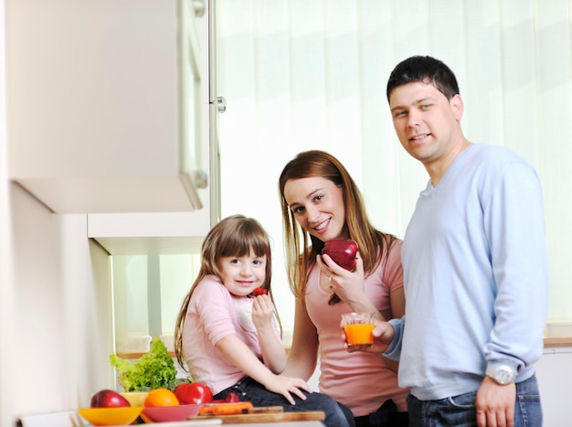 une jeune famille heureuse prend l'heure du déjeuner avec des fruits et des légumes frais dans une cuisine lumineuse