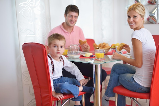 une jeune famille heureuse prend un petit-déjeuner sain dans la cuisine avec des détails rouges sur la lumière du matin