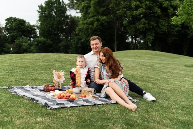 Une jeune famille heureuse s'amuse au pique-nique. pama maman et son fils marchent dans la nature. fils sur la poitrine de son père. la famille se trouve sur l'herbe dans le parc. vacances en famille