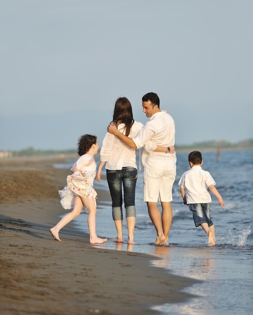 une jeune famille heureuse s'amuse sur la plage et saute au coucher du soleil