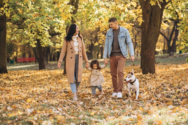 Une jeune famille heureuse se promène et joue avec un chien dans le parc en automne