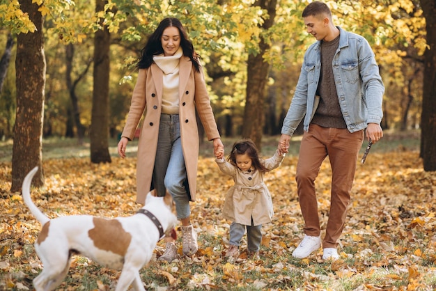 Une jeune famille heureuse se promène et joue avec un chien dans le parc en automne