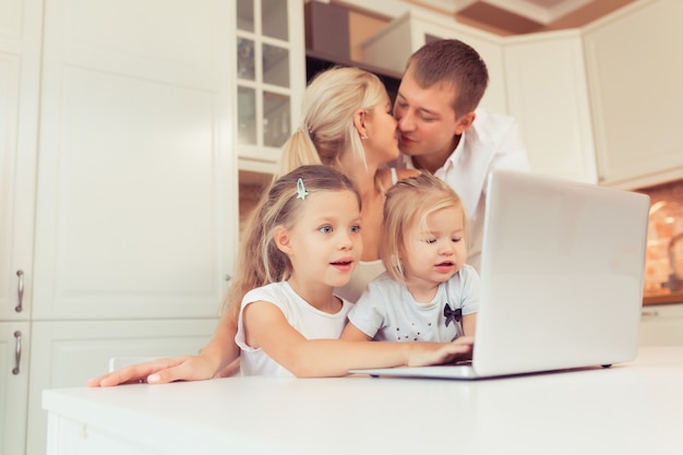 Jeune famille heureuse utilisant un ordinateur portable assis dans la cuisine à la maison