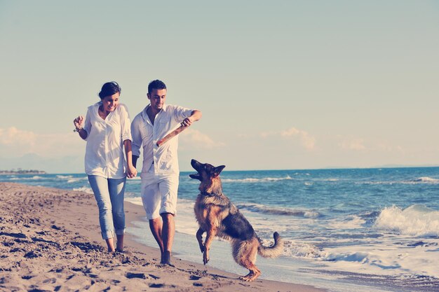 une jeune famille heureuse en vêtements blancs s'amuse et joue avec un beau chien en vacances sur une belle plage