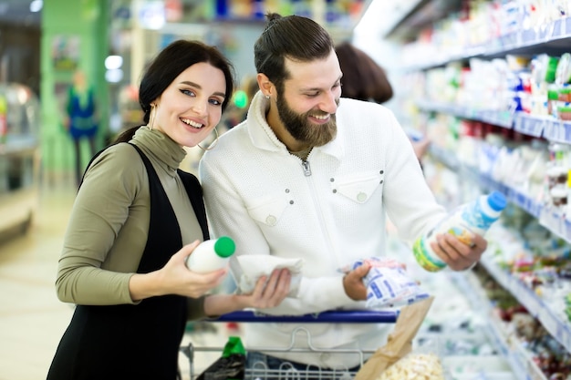 Une jeune famille, un homme et une femme choisissent du lait dans un grand supermarché.