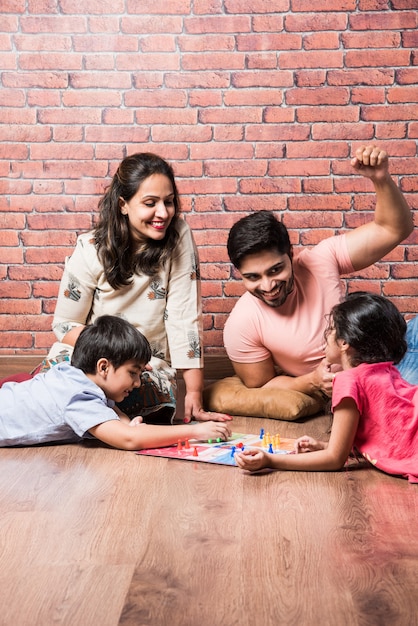 Jeune famille indienne de quatre personnes jouant à des jeux de société comme Chess, Ludo ou Snack and Ladder à la maison en quarantaine