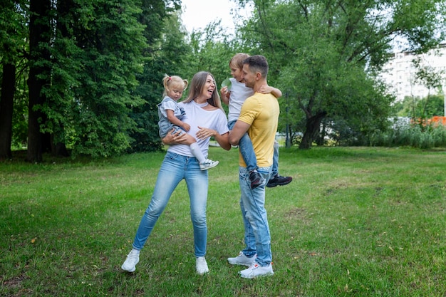 Une jeune famille en jeans et T-shirts blancs joue avec de petits enfants dans un parc d'été vert par une journée ensoleillée