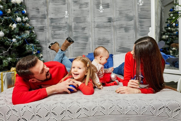 Jeune famille sur le lit avec des enfants sur le fond de l'arbre de Noël