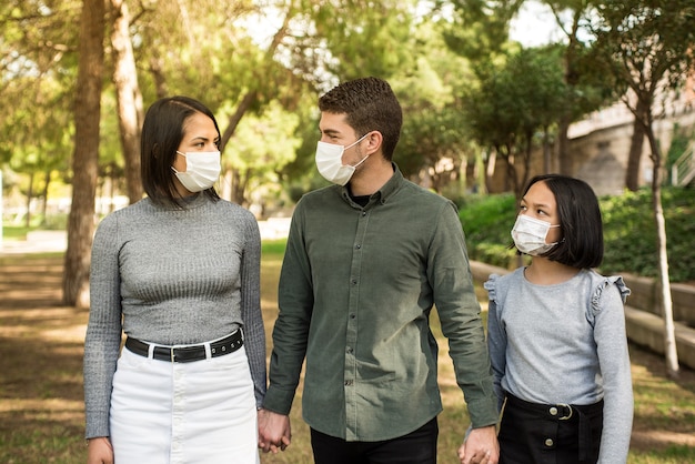 Une jeune famille marchant dans le parc porte un masque chirurgical lors d'une infection à coronavirus.