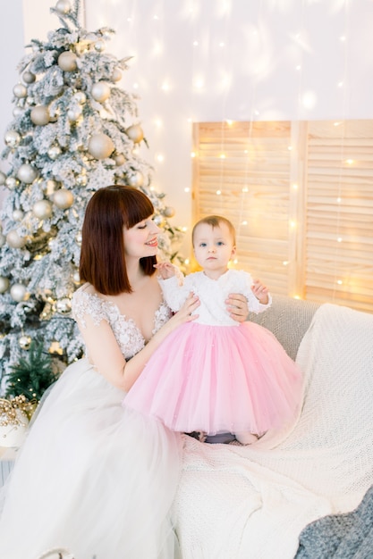 Jeune famille, mère avec bébé fille, assis sur le canapé, sur le fond de l'arbre de Noël