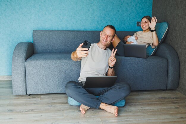 Jeune famille mère père et fille passent du temps ensemble dans le salon Style de vie d'une famille se détendant dans un appartement tandis qu'un homme travaille derrière avec un ordinateur portable et une femme et sa tablette