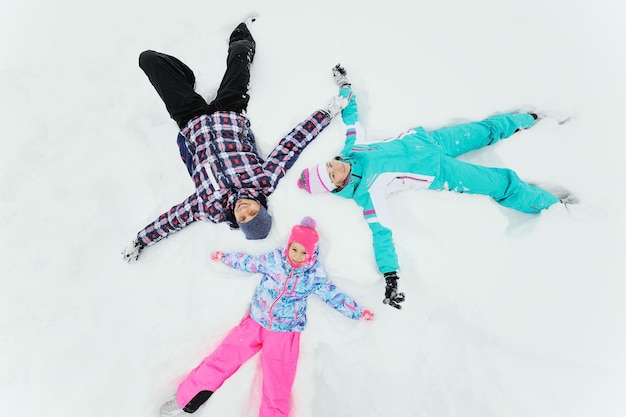 Une jeune famille- mère, père et petite fille en combinaisons de ski colorées s'amusant allongé sur la neige. Plaisirs d'hiver