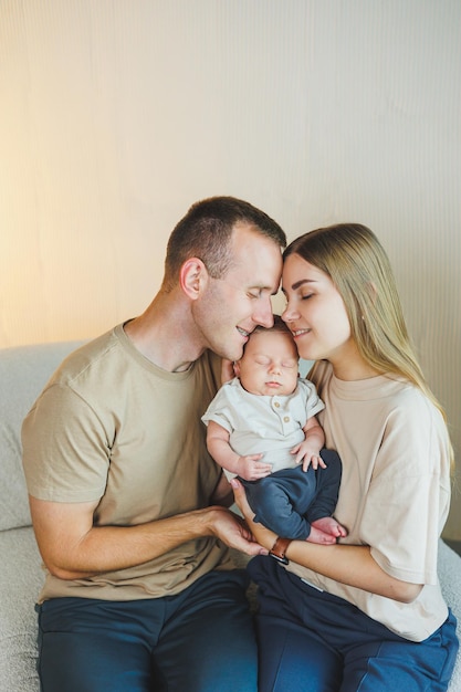 Une jeune famille avec un nouveau-né, une mère et un père heureux embrassant leur enfant, des parents et un enfant souriant dans leurs bras.