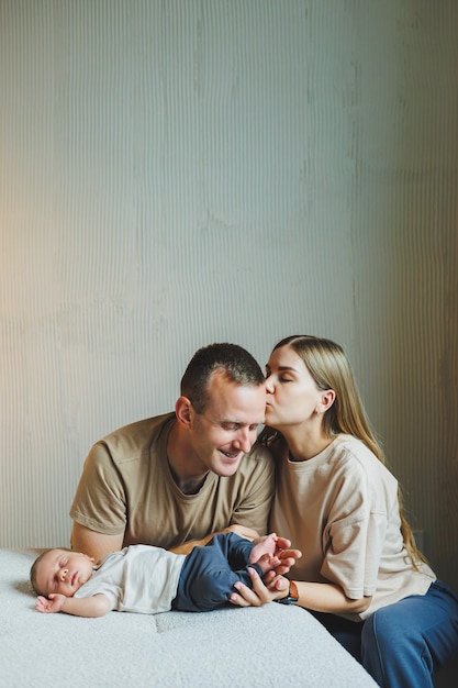 Une jeune famille avec un nouveau-né, une mère et un père heureux embrassant leur enfant, des parents et un enfant souriant dans leurs bras.