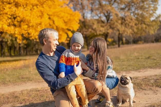 Une jeune famille avec un petit enfant et un chien passent du temps ensemble pour une promenade dans le parc en automne.