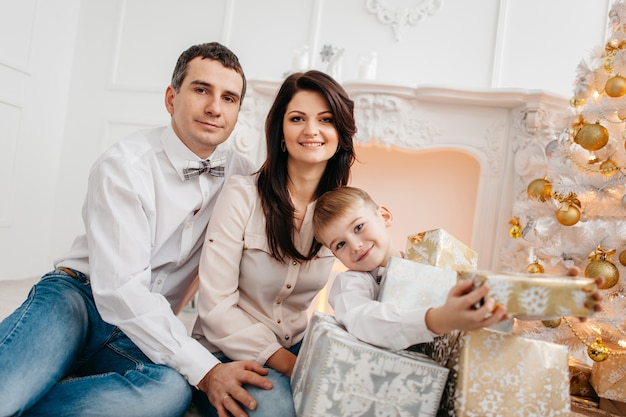 Jeune famille près de la cheminée blanche avec des cadeaux de Noël