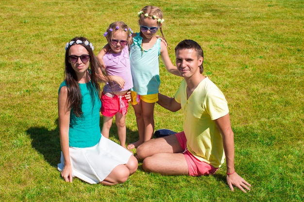 Jeune famille de quatre personnes assises sur l'herbe et s'amuser