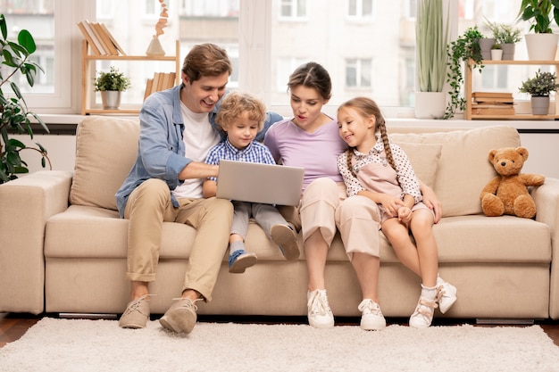 Jeune famille de quatre personnes avec ordinateur portable surfer sur le net tout en choisissant le film
