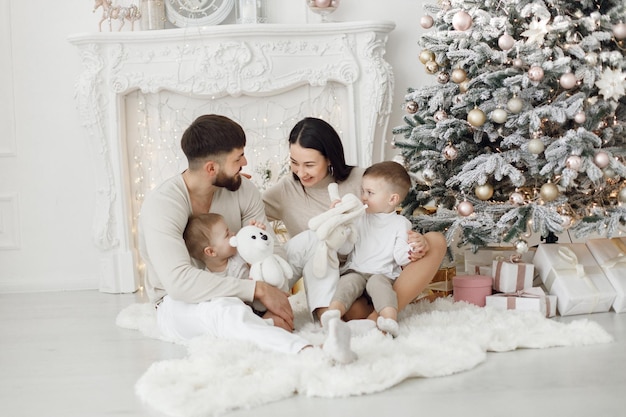 Jeune famille en vêtements blancs assis près de l'arbre de Noël